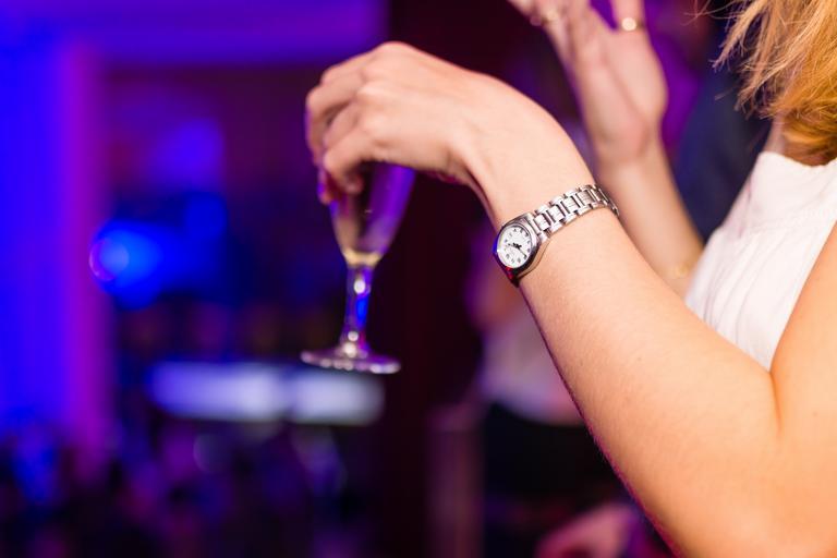žena v klubu, v ruce drží skleničku s pitím, má hodinky a bílou halenku